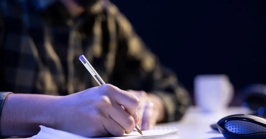 A man is engaged in writing on a piece of paper using a pen.